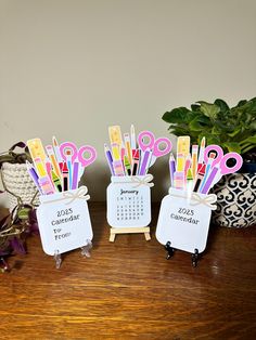 three office supplies sitting on top of a wooden table next to a potted plant