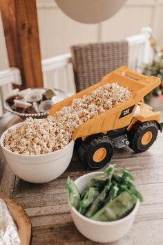 a toy dump truck filled with popcorn sitting on top of a table next to a bowl