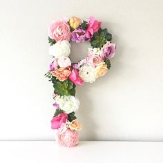 the letter p is made up of flowers and greenery on a white surface with a wall in the background