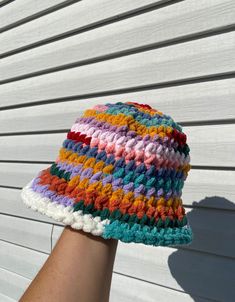 a woman's hand is holding a multicolored crocheted bucket hat