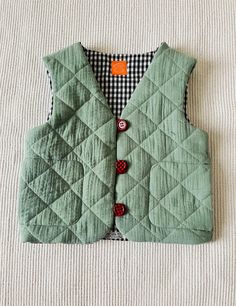 a green vest sitting on top of a white bed next to a black and white checkered pillow