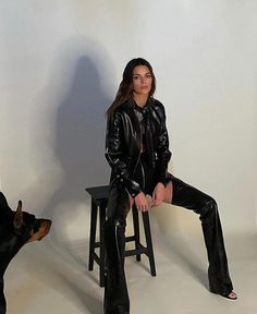 a woman sitting on top of a stool next to a black dog and wearing boots