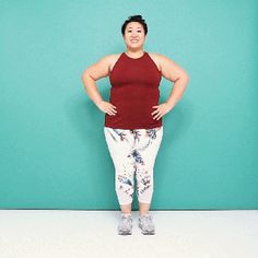 a woman standing in front of a blue wall wearing leggings and a tank top