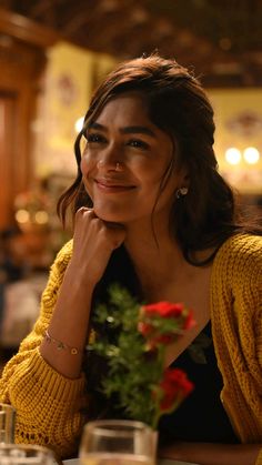 a woman sitting at a table with a flower in her hand and looking to the side