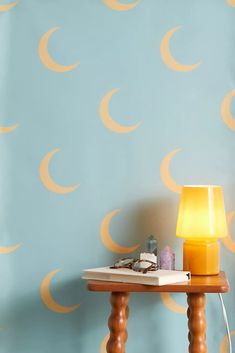 a wooden table topped with a lamp next to a blue wall covered in yellow crescents