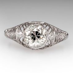 Circa 1920s domed ring features a pierced design and is centered with one (1), bezel set, old European cut diamond. The gallery is accented with six (6), bead set, round single/Swiss cut diamonds. The ring measures 9.8mm at the top, rises 7.0mm above the finger, tapering to 2.0mm wide and 1.2mm thick at the base of the shank. Art Deco Diamond Ring With Bezel Setting, Art Deco Diamond White Ring With Bezel Setting, Art Deco White Diamond Ring With Bezel Setting, Art Deco White Gold Diamond Ring With Bezel Setting, Vintage White Gold Diamond Ring With Bezel Setting, Vintage Round Diamond White Filigree Ring, Classic Domed Bezel-set Jewelry, Vintage Diamond Ring With Bezel Setting, Vintage Diamond Ring With Bezel Setting And Round Band