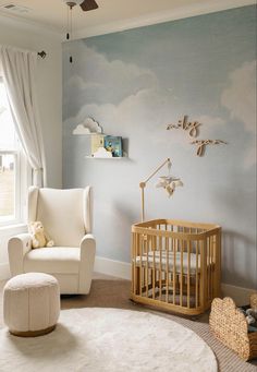 a baby's room with a chair, crib and wall mural