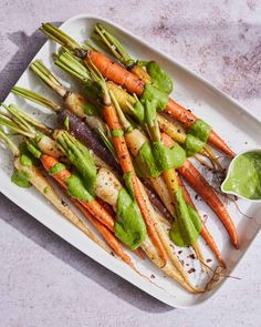 carrots and asparagus on a white platter with a green dipping sauce