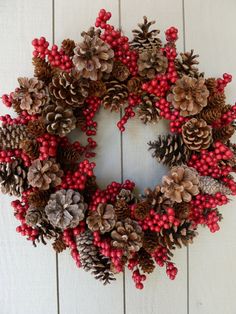 a wreath with pine cones and berries hanging on a wall next to a red frame