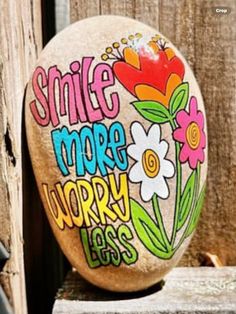 a painted rock with the words smile more worry less on it, sitting next to a wooden fence