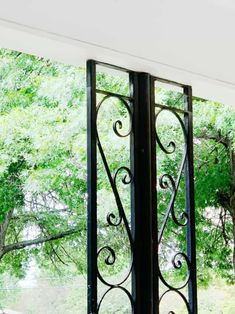 an open window with wrought iron designs on the outside and inside, looking out onto a wooded area