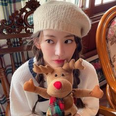 a young woman holding a stuffed reindeer in her hands while wearing a hat and scarf