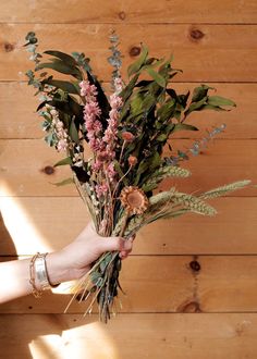 a person holding a bouquet of flowers in their hand on a wooden wall with wood planks