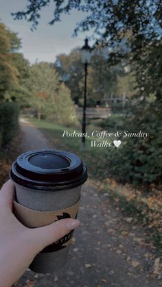 a person holding a coffee cup in their hand on a path with trees and grass