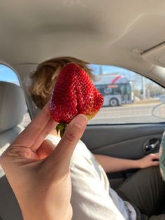 a person holding up a strawberry in the back seat of a car