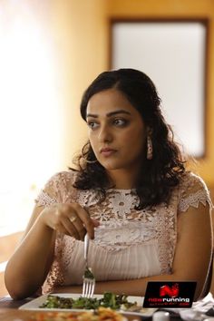 a woman sitting at a table with a plate of food and fork in her hand