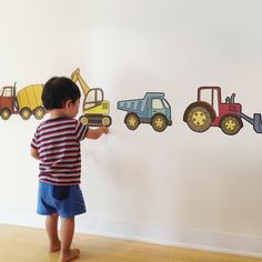 a little boy standing in front of a wall with construction vehicles on it