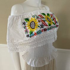 "Mexican Off shoulder elastic top with colorful sunflower embroidery. Made out of manta, 100% cotton. Color- Black/ Red and green floral embroidery. Please note: each piece is unique, the embroidery on the top and belt may be slightly different from the one pictured. Dimensions: Small Bust- 39\" Length- 20\" Medium Bust- 42\" Length- 20\" Made in Chiapas, Mexico. 🧺Care Instructions: We recommend hand washing, lay flat to dry. 📲Feel free to contact us with any questions you may have!  🛍More co White Hippie Peasant Top For Summer, White Hippie Peasant Top For Festival, Cotton Folk Peasant Top For Beach, Folk Style Cotton Peasant Top For Beach, White Cotton Festival Peasant Top, Fitted Cotton Peasant Top With Embroidery, White Cotton Peasant Top For Festival, Summer Hippie Embroidered Peasant Top, White Embroidered Hippie Tops