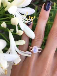 a close up of a person's hand with a ring and flowers in the background