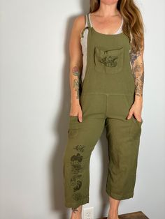 Super cute and comfy, these oversized olive green overalls will become an instant favorite. Tie closure, front and side patch pockets. Printed on both front and back legs  and chest pocket with our hand-drawn mushroom designs. Available in S/M, L/XL and XXL. Model is a women's medium/large and wearing a S/M.  50% Viscose, 30% Hemp, 20% Cotton, ethically made. Machine wash cold. Tumble dry low or line dry. Green Bib Front Overalls With Pockets, Casual Cotton Cargo Style Overalls, Green Bib Front Jumpsuit With Pockets, Green Jumpsuit With Pockets And Bib Front, Green Casual Cotton Overalls, Casual Green Cotton Overalls, Casual Khaki Jumpsuits And Rompers With Side Pockets, Green Cotton Utility Overalls, Casual Green Jumpsuits And Rompers With Side Pockets