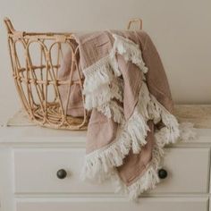 a basket sitting on top of a white dresser next to a pink and white blanket