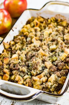 a casserole dish with meat and vegetables in it on a table next to apples