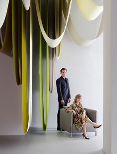 a man and woman sitting on a chair in front of a wall with hanging lights