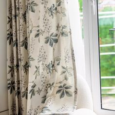 a white chair sitting in front of a window next to a curtain with flowers on it