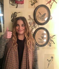 a woman standing in front of a wall with pictures on it and giving the thumbs up