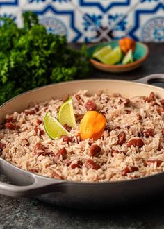 a pan filled with rice, beans and limes on top of a table next to some parsley