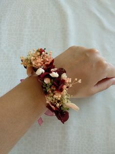 a woman's arm wearing a bracelet with flowers and leaves on it, sitting on a bed