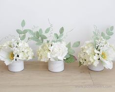 three vases filled with white flowers and greenery