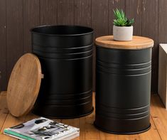 two black trash cans sitting on top of a wooden floor next to a potted plant