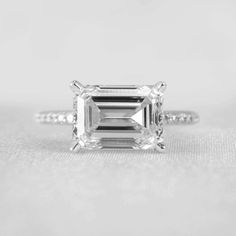 an emerald cut diamond ring with two diamonds on the band and side stones in rose gold