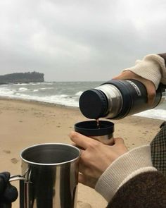 a person holding a coffee cup and looking at the ocean with a camera in their hand