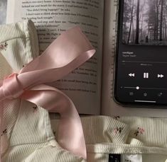 an open book with a pink ribbon on it next to headphones and a cell phone