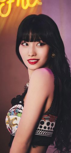 a woman with long black hair and red lipstick posing in front of a neon sign