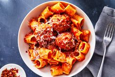 a white bowl filled with pasta and meatballs next to a fork on a table