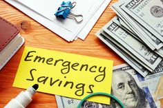 a pile of money sitting on top of a table next to a yellow sign that says emergency savings