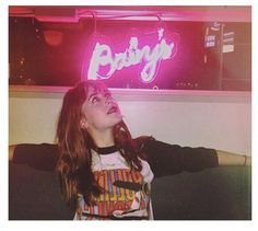 a woman sitting in front of a neon sign with the word baby on it's back