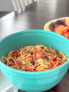 a blue bowl filled with pasta and vegetables on top of a table next to fruit