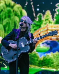 a woman with blonde hair and sunglasses playing an acoustic guitar on stage at a concert