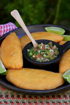 fried fish sticks with salsa and lime wedges on a black plate next to a red checkered napkin