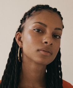 a close up of a person with braids and an earring in front of a white wall