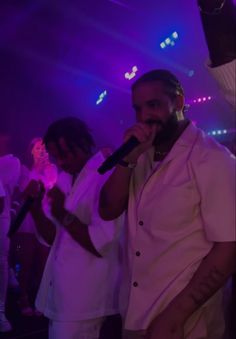 two men singing into microphones in front of purple lights and people watching from the sidelines