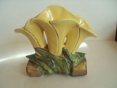 a yellow vase with two bananas on it's side sitting on top of a tree stump