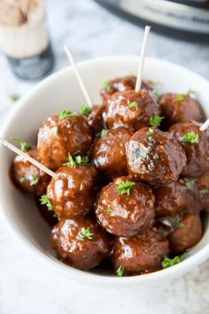 a white bowl filled with meatballs covered in sauce and parsley on toothpicks