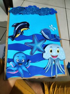 a child holding up a cardboard box with sea animals on it and an octopus in the middle