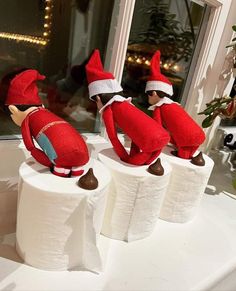 three elfs are sitting on top of toilet paper rolls in the window sill