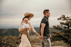 a man and woman walking with a baby in their arms on top of a mountain